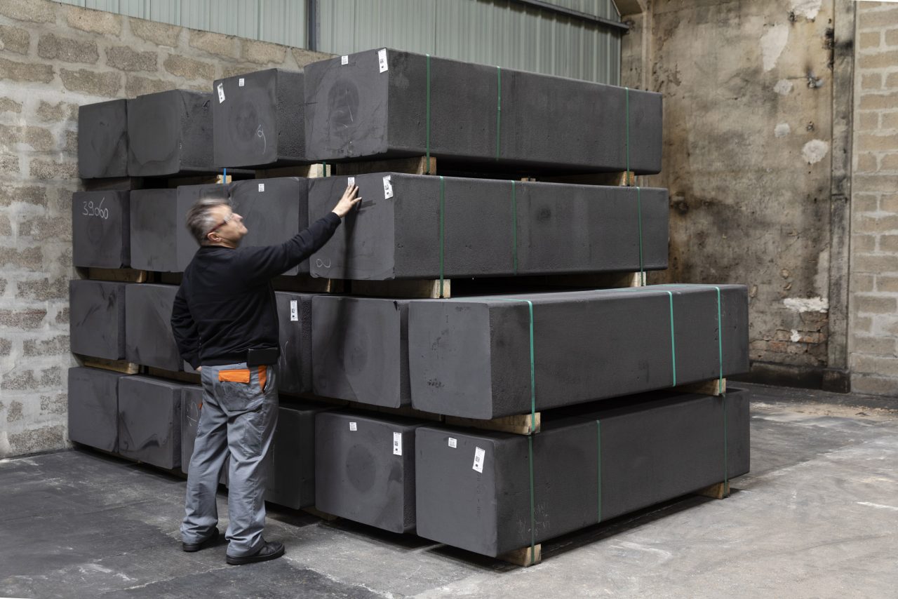 Ouvrier contrôlant un stock de barres de graphite dans un atelier de production.